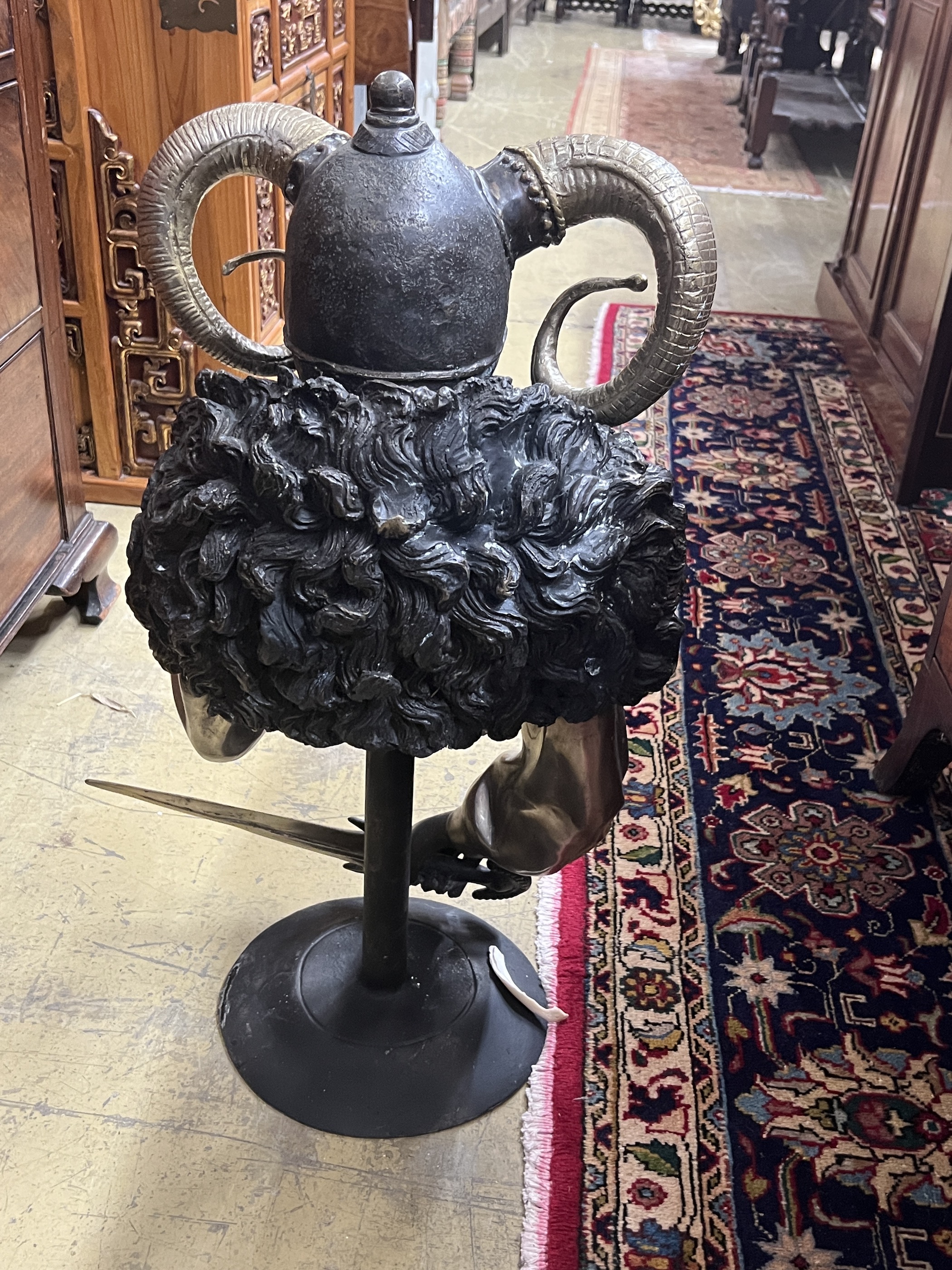 A patinated and polished metal masked female warrior bust on stand, height 70cm